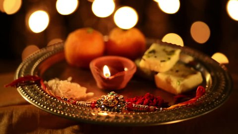 Locked-on shot of a spinning puja thali with rakhi, sweets and oil lamp