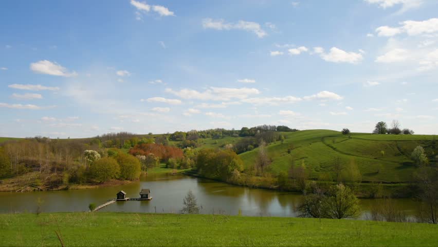 clouds timelapse of lake with water houses in spring fields and forest landscape