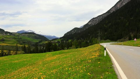 ST. MORITZ, SWITZERLAND - MAY 2012: Zoom in shot of vehicles passing through a flower field, St. Moritz, Engadine Valley, Switzerland