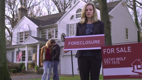 MS, Real estate agent holding FORECLOSURE sign, couple in background
