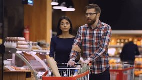Happy young couple walking in supermarket and puts something in their shopping trolley