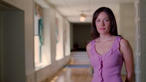Full-face portrait of a dark-haired young woman standing in a long corridor