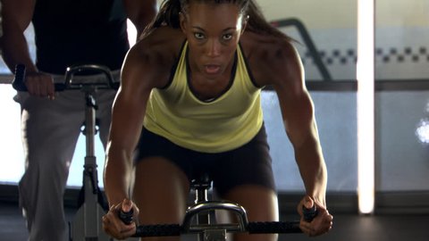 Tilt-up from wheel of stationary bicycle to woman cycling in spinning class