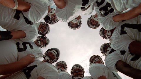 Football players in a huddle, camera looking up from center