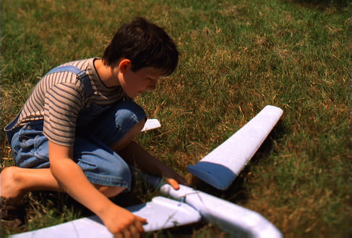 Young boy kneeling on grass while building a toy airplane