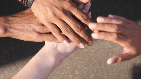 Arm of all races and colors stacked together one by one in unity and teamwork and then raised. Many multiracial hands getting together in the center of a circle and then cheer. Close up outdoor shot