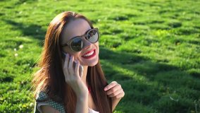 Beautiful smiling woman in glasses sitting on the grass and doing selfie,using mobile phone,texting.Sunset sun,Full HD close-up, retro vintage style with sunglasses