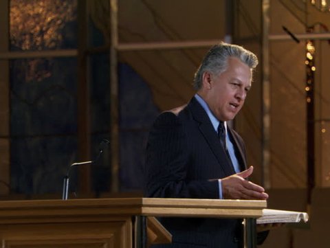 Pastor speaking from pulpit with stained glass window in background
