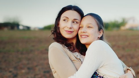 Mama gently hugs her daughter for 11 years. Together they look in one direction to the setting sun. Family values