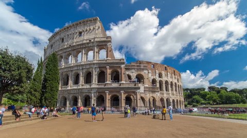 Many tourists visiting The Colosseum or Coliseum timelapse hyperlapse, also known as the Flavian Amphitheatre in Rome, Italy. Cloudy blue sky. Zoom in