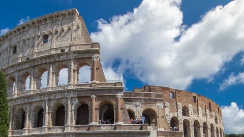 Many tourists visiting The Colosseum or Coliseum timelapse hyperlapse, also known as the Flavian Amphitheatre in Rome, Italy. Cloudy blue sky. Zoom out
