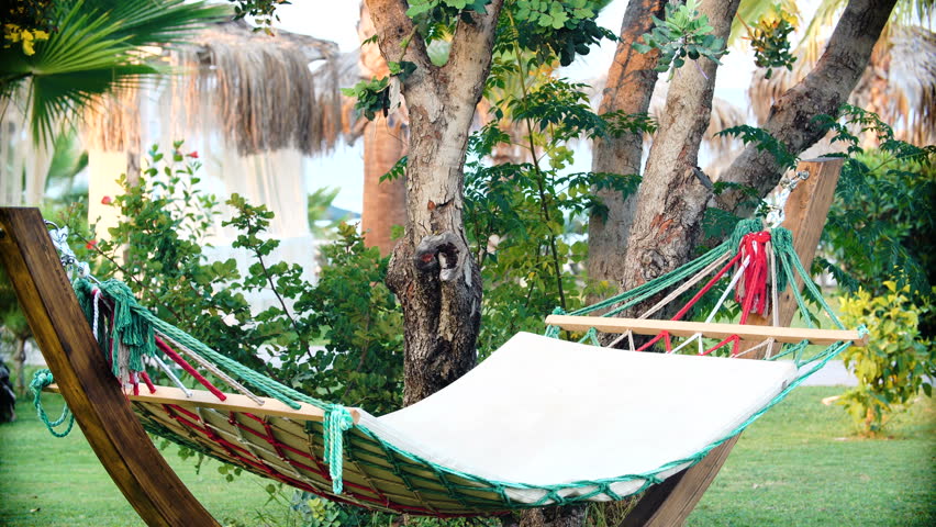young brunette woman in hat relaxed in hammock on tropical beach