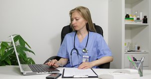 Busy Clinician Doctor Woman Typing At Laptop Writing Clipboard Data In Healthcare Room