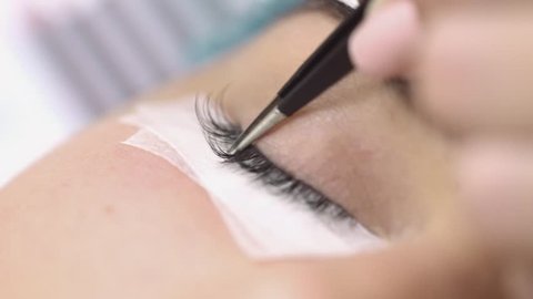 Eyelash extension,makeup artist takes with forceps and stick artificial lashes on the woman's eye,extreme close up,studio beauty,professional procedures eyelash extensions,no color grading,indoors.