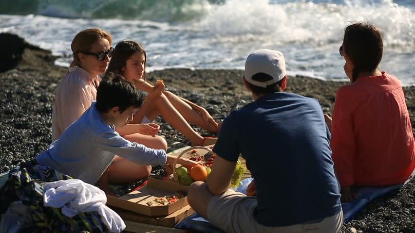 Friends with children eating pizza on the beach. Picnic by the sea on the beach