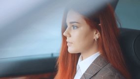Red-haired amazing model red-haired girl in brown jacket and white t-shirt with deep aqua blue eyes sitting in car and using her smartphone Steadicam slow motion video