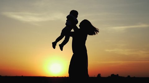 Happy child rushes into hands of mother. Family hugs over sunset sky background. Silhouettes of anonymous boy and woman outside in summer or autumn landscape. Slow motion 180fps