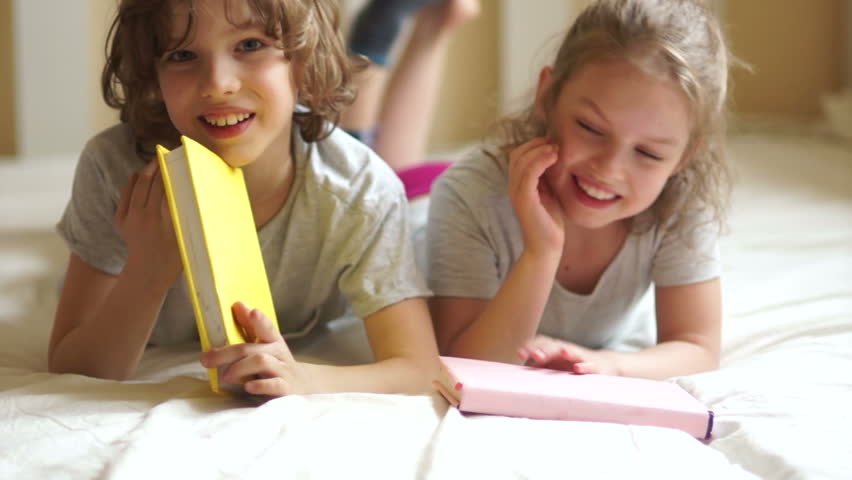 Children playing in the bedroom. On the bed are books. They hit heads together.The girl hurt, she covers her face with her hands. Brother and sister, boy and girl. To cry, to hurt.