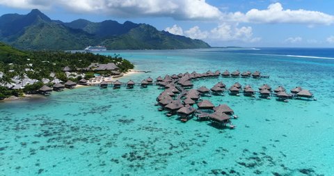 Tropical vacation paradise island with overwater bungalows resort in coral reef lagoon ocean by beach. Aerial video of Moorea, French Polynesia, Tahiti, South Pacific Ocean.