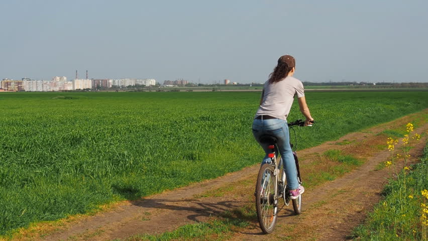 Girl on a bicycle in the nature. A woman is riding a bicycle outside the city. Rapeseed field. Country road. Slow motion.