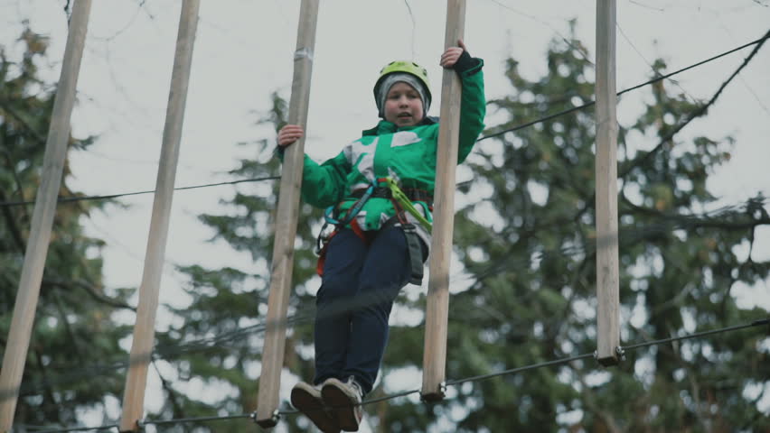 young boy passing the cable route high among trees, extreme sport in adventure park