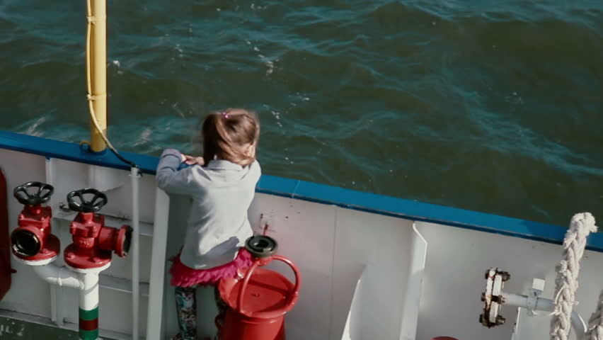 A little girl is standing closely to the board of a ship deck and looking at the water