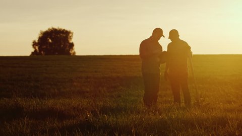 Two American farmers communicate in the field at sunset. Next to them is a shovel