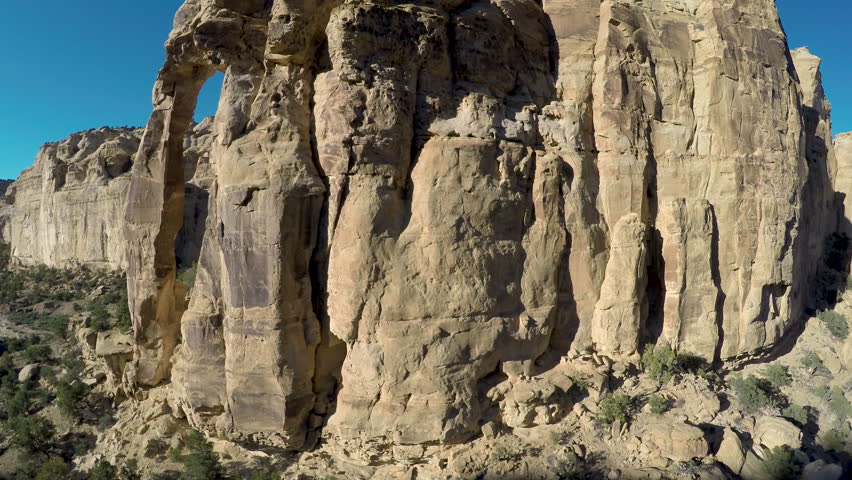 Aerial-Flying over rugged sandstone monolith of Eagle Canyon Arch reveals fortress-like rock formation in the San Rafael Swell desert beyond on a sunny day with a clear blue sky