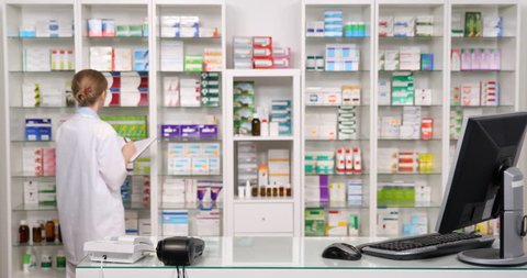 Serious Pharmacist Woman Analyzing Drugs Shelf Agenda Noting Computer Searching