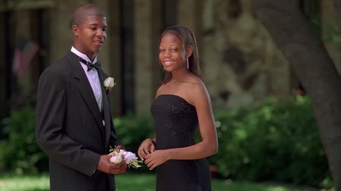 Young man in tux giving wrist corsage to girl in prom gown