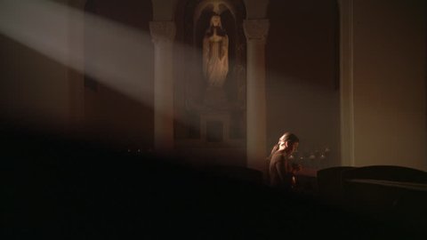Woman kneeling in ray of sunlight in Catholic church