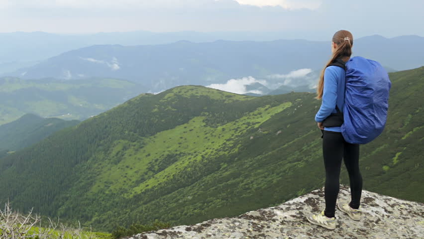 Woman with backpack standing on the edge of the stone looks into the distance

