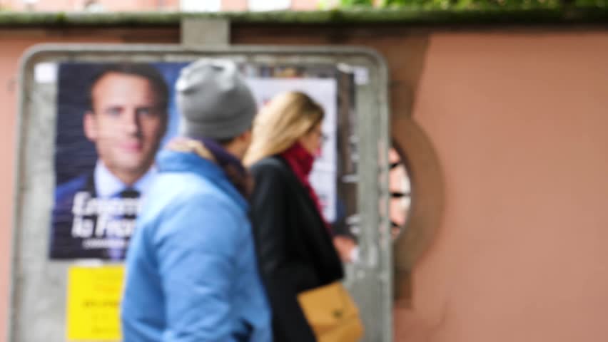 Unrecognizable people walking in front of the defocused Presidential candidates posters for French presidency in French city