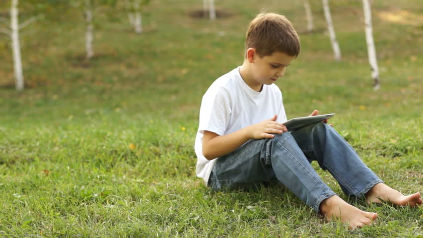 Boy using a tablet pc and sitting on the grass
