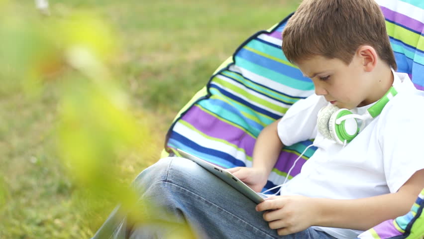 Boy online with a tablet pc sitting in a chair outdoors.