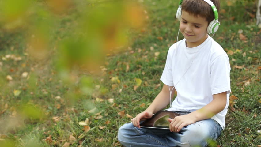 Boy with tablet computer sitting on the grass gives thumbs up