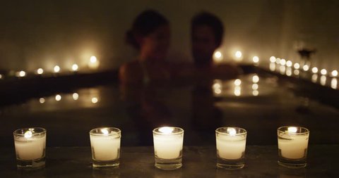 Young couple relaxing in romantic candlelit hot tub jacuzzi spa resort at night in private hotel room terrace. Romantic honeymoon getaway travel vacation adults enjoying their holidays.