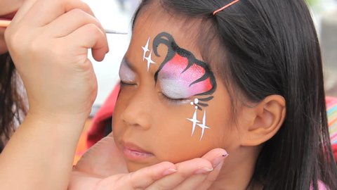 A cute little 6 year old Asian girl smiles after receiving her face painting mask at the summer carnival.