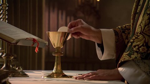Hands of priest with wafer and chalice during Eucharist