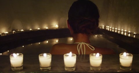 Relaxation and luxury at spa jacuzzi hot tub. Woman taking a bath at night by candlelights outside.