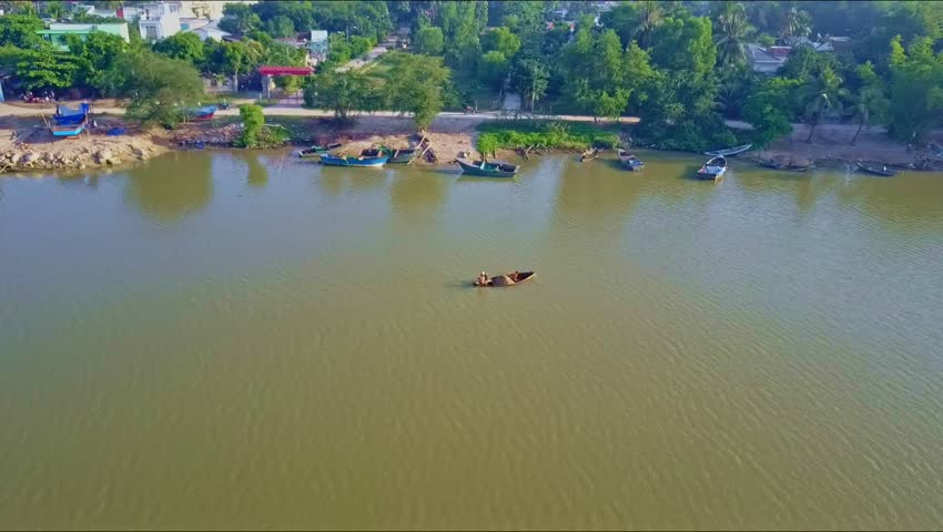 aerial view small wooden boat sails on green calm river surface to piers against bank with road and trees