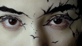 Fashion close-up slow motion portrait of model female with a amazing creative make-up. Painted muah silhouettes of trees and birds. Calm face, halloween. Dark background. Effectively opens her eyes. - Powered by Shutterstock - Get 15% off with code: PIKWIZARD15