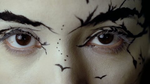 Fashion close-up slow motion portrait of model female with a amazing creative make-up. Painted muah silhouettes of trees and birds. Calm face, halloween. Dark background. Effectively opens her eyes.