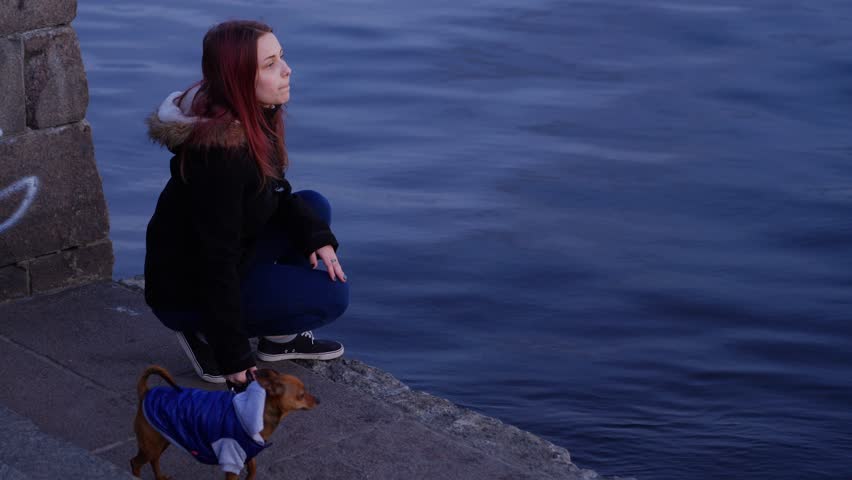 Teen girl with a little dog on a night street near river.