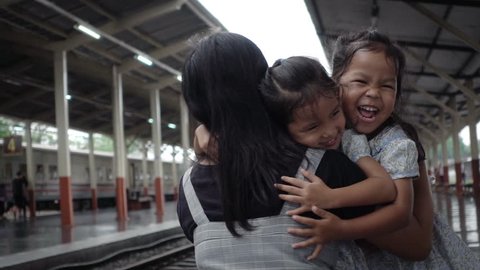 Two cute asian little girls are running to give a hug with their mother on railway station