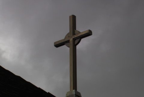 Wooden cross on roof with gray time-lapse clouds drifting above