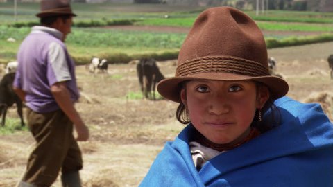 Ecuadorean farm girl in brown hat; adults feeding cattle in background