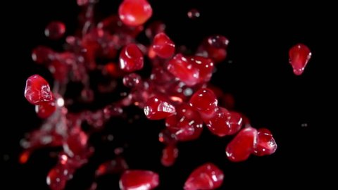 Red ripe garnet grains with juice fly to the camera on a black background in slow motion