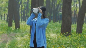 VR headset on woman outdoors. Portrait of brunette lady wearing VR glasses. Virtual reality helmet on caucasian woman in park or forest. VR headset on attractive girl in blue coat.