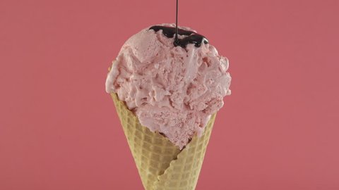 Strawberry ice cream with chocolate sauce in waffle cone on pink background